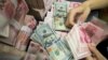 A Chinese bank employee counts 100-yuan notes and US dollar bills at a bank counter (Photo by AFP)