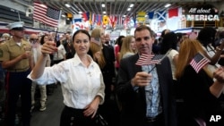 Nuevos ciudadanos estadounidenses ondean banderas durante una ceremonia de naturalización a bordo del USS Bataan el 7 de mayo de 2024 en Miami.
