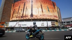 Un hombre pasa en motocicleta junto a un cartel que muestra misiles balísticos iraníes en servicio en Teherán el 19 de abril de 2024.