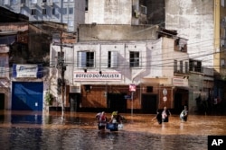 People wade through an area flooded by heavy rains in Porto Alegre, Rio Grande do Sul state, Brazil, Monday, May 6, 2024. (AP Photo/Carlos Macedo)