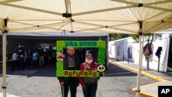 Una pareja posa para una foto sosteniendo un marco con un mensaje que dice: "Tercera dosis, vacúnese, refuerzo", luego de recibir un refuerzo de AstraZeneca durante una campaña de vacunación para personas de 60 años y más, en Ciudad de México, el 4 de enero de 2022.