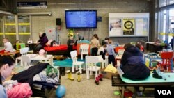 Área de juegos para niños instalada en una estación de trenes de Varsovia, Polinia. La televisión está mostrando dibujos animados ucranianos. [Jamie Dettmer/VOA]
