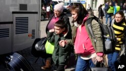 Refugiados ucranianos con niños abordan el transporte en una plaza junto a una estación de tren en Przemysl, Polonia, el martes 22 de marzo de 2022. [Foto AP/Sergei Grits]