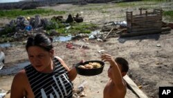Andrea Calisti sostiene un molde de pan dulce donado mientras su hijo Nathanael de 7 años toma un pedazo, entregado por miembros de la organización social Movimiento de Trabajadores Excluidos en el barrio 17 de Octubre de Buenos Aires, el 2 de febrero de 2022. 