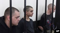 Dos ciudadanos británicos, Aiden Aslin (izq.) y Shaun Pinner (der.), y el marroquí Saaudun Brahim, (centro), tras las rejas en un tribunal en Donetsk, bajo el control del autoproclamado Gobierno de la República Popular de Donetsk, en el este de Ucrania, el 9 de junio de 2022.