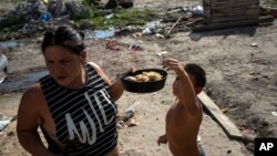 Andrea Calisti sostiene una bandeja de pan dulce donado mientras su hijo Natanael, de 7 años, alcanza un pedazo, en el barrio 17 de Octubre de Buenos Aires, Argentina, el 2 de febrero de 2022. 
