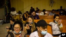 La gente espera y habla con familiares por teléfono en un almacén administrado por el grupo sin fines de lucro Mission: Border Hope, en Eagle Pass, Texas, el 23 de mayo de 2022.