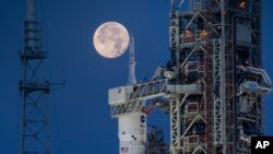 Se ve una luna llena detrás del Sistema de Lanzamiento Espacial Artemis I (SLS) y la nave espacial Orion, encima del lanzador móvil, lista para un ensayo generalen el Complejo de Lanzamiento 39B en el Centro Espacial Kennedy de la NASA en Florida, EEUU, el 14 de junio de 2022. 
