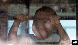 Un niño inmigrante mira desde un autobús de la Patrulla Fronteriza de EE.UU. mientras manifestantes bloqueaban la calle frente al Centro de Procesamiento Central de la Patrulla Fronteriza de los Estados Unidos el sábado 23 de junio de 2018 en McAllen, Texas.