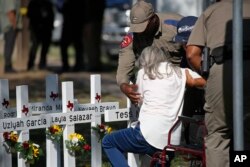 Los policías ayudan a una mujer después de presentar sus respetos frente a las cruces con los nombres de los niños asesinados esta semana en la Escuela Primaria Robb en Uvalde, Texas, el jueves 26 de mayo de 2022.