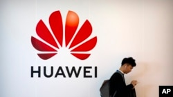 ARCHIVO - En esta fotografía de archivo del 31 de octubre de 2019, un hombre usa su teléfono inteligente cerca de una valla publicitaria de la empresa de tecnología china Huawei en la PT Expo en Beijing.