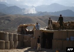 ARCHIVO - Policías afganos miran hacia el horizonte donde una columna de humo se levanta luego de un ataque a posiciones de militantes del Estado Islámico en un punto de control en la oriental provincia de Nangarhar. Julio 7, 2018.