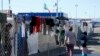 Migrantes caminan junto a la cerca de un campamento improvisado que bloquea la entrada a un cruce peatonal a Estados Unidos el 8 de noviembre de 2021, en Tijuana, México.