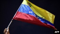 Un hombre muestra una bandera nacional mientras familiares y amigos de migrantes venezolanos que murieron cuando se hundió un barco que los transportaba a Trinidad y Tobago, protestan en Güiria, Venezuela, el 18 de diciembre de 2020.