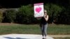 Una manifestante afuera del Club Nacional de Golf Trump, sostiene un cartel que dice "Amo a los informantes" mientras pasa la caravana del presidente de EE.UU. Donald Trump, de camino a la instalación en el norte de Virginia. Sterling, VA. Domingo 29 de septiembre de 2019.
