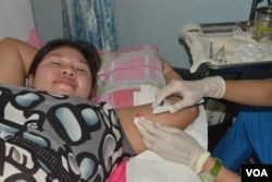 A woman receives a free implant contraceptive at Likhaan Women's Health Center. She says her family cannot afford to raise more than the three children they have in Manila, Aug. 6, 2015. (Photo: Simone Orendain / VOA)