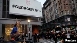 Personas gritan desde un vehículo, en Boston, Massachusetss, mientras otros marchan bajo un rótulo con el nombre de George Floyd, quien murió bajo custodia de la policía de Minneapolis. 