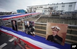 Cerca de los retratos (der. a izq.), de John S. McCain, John S. McCain, Jr. y John S. McCain III, el secretario de la Marina Richard Spencer y su esposa Polly Spencer desembarcan del USS John S. McCain después de una ceremonia de rededicación en la Base naval estadounidense de Yokosuk, en el sureste de Tokio, el 12 de julio de 2018.