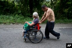 El migrante hondureño Omar Orella empuja a su compañera Nery Maldonado Tejeda en una silla de ruedas, mientras viajan con cientos de otros hondureños que se dirigen a EE.UU., cerca de Chiquimula, Guatemala, el martes 16 de octubre de 2018.