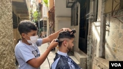 En un callejón del barrio caraqueño La Lucha, Jackner Quevedo atiende a un cliente en una improvisada barbería frente a su casa. Septiembre, 2021. Foto: Adriana Nuñez Rabascall - VOA.