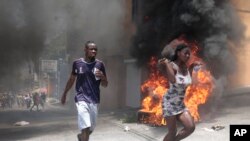 Manifestantes pasan corriendo junto a neumáticos incendiados durante una protesta contra la inseguridad en Puerto Príncipe, Haití, el 7 de agosto de 2023.