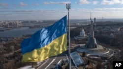 La bandera nacional de Ucrania, coronada con un símbolo de tridente, ondea sobre la capital con el Monumento a la Patria a la derecha, en Kiev, el 13 de febrero de 2022. 