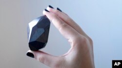 An employee of Sotheby's Dubai presents a 555.55 Carat Black Diamond "The Enigma" to be auctioned at Sotheby's Dubai gallery, in Dubai, United Arab Emirates, Monday, Jan. 17, 2022. 