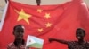 在中国资助的有千所住房单位的吉布提建筑工程启动仪式之前，拿着吉布提国旗的小男孩站在巨大的中国国旗前。（2018年7月4日）