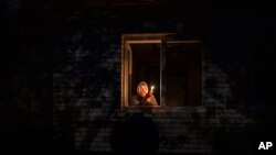 ARCHIVO - Catherine, de 70 años, mira por la ventana mientras sostiene una vela para iluminar el interior de su casa durante un corte de energía, en Borodyanka, región de Kyiv, Ucrania, el jueves 20 de octubre de 2022. (AP)