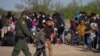 Migrantes centroamericanos con niños esperan en un campo de béisbol después de cruzar el Río Grande hacia EE. UU. en balsas, en La Joya, Texas, el 19 de marzo de 2021.