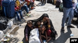 Una mujer cubre a sus hijos con un chal para protegerlos del sol mientras espera con otros trabajadores migrantes y familias para registrarse en un tren que va a sus lugares de origen.
