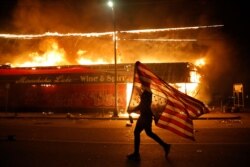 Un manifestante lleva una bandea de EE.UU. invertida, una señal de angustia, frente a un edificio en llamas el 28 de mayo de 2020 en Minneapolis, en protesta por la muerte de George Floyd.